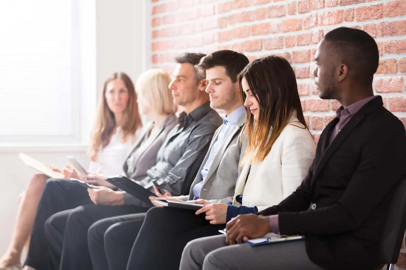 People sitting and waiting against a brick wall