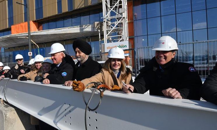 Several people with hard hats standing behind last beam to be placed in construction of Markham campus